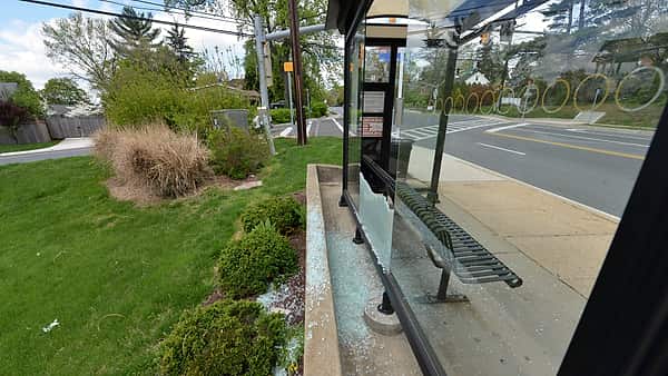 Shattered safety glass scattered across the concrete floor of a roadside bus shelter beside an empty bench