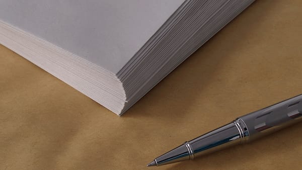 A silver rollerball pen resting on tan paper beside the corner of a thick stack of white sheets