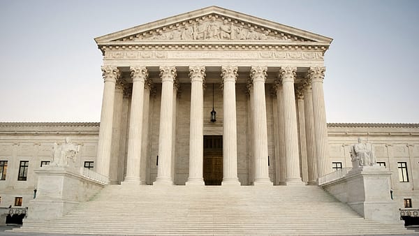 A white marble building front with tall fluted columns, a carved pediment, and a wide flight of steps
