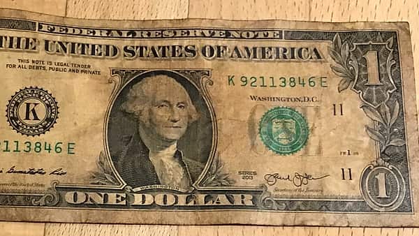 A creased and worn one dollar bill lying face up on a light wooden tabletop