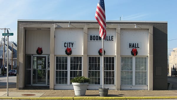 A single-story white municipal building with block letters across its front and a flag flying from a tall pole