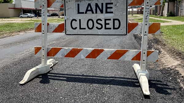 An orange and white striped barricade standing across a paved road under a sign reading LANE CLOSED