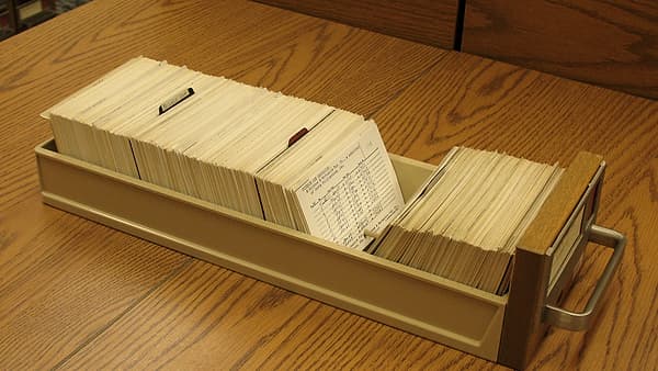 An open beige metal card drawer packed with handwritten index cards sitting on a polished oak table