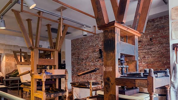 Two large wooden hand-operated printing presses in a workshop with exposed brick walls and timber beams