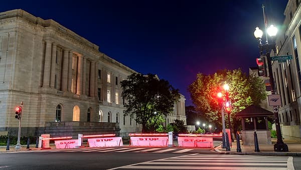 A columned stone building floodlit at night behind a row of red-lit street barriers marked STOP