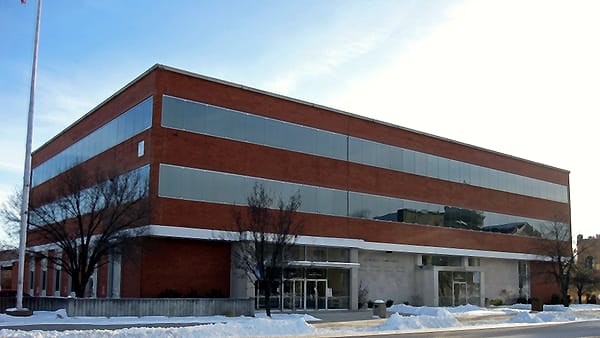 A three-story brick and glass office block with a bare flagpole and snow piled along the curb