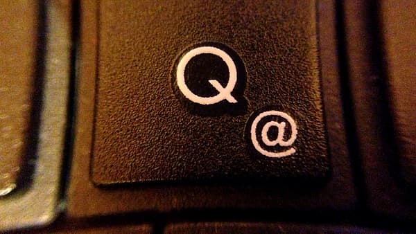 A macro view of one black keyboard key marked with a white Q and an at sign, neighboring keys blurred
