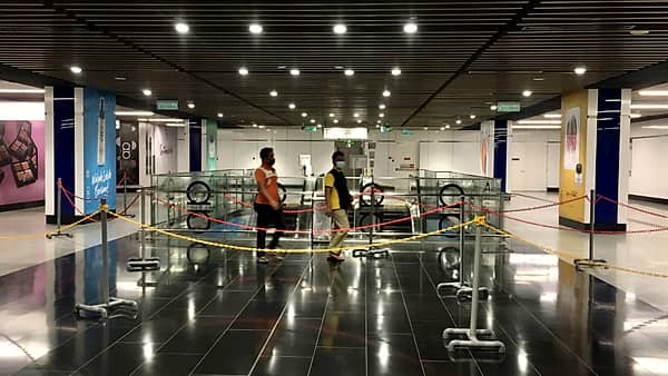 Metal queue barriers funnelling toward a bank of fare gates at a station entrance.