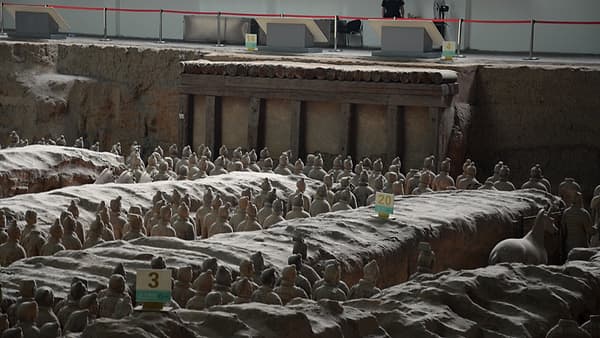 Rows of life-size clay warrior figures standing in long earthen trenches inside a covered excavation pit