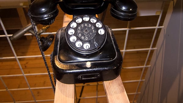 An old black rotary dial telephone with its handset on the cradle, sitting on a pale wooden sawhorse