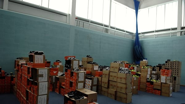 Stacks of orange and kraft shoe boxes with loose sneakers piled across the floor of a pale blue gym hall