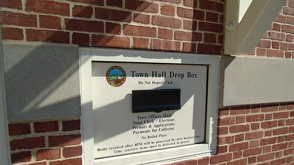 A metal drop box set into a red brick wall beneath a white sign reading Town Hall Drop Box