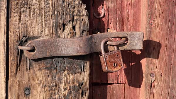 A rusted iron hasp and padlock fastened across weathered wooden boards, one plank bare and the next faded red