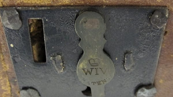 A close view of an old iron lock plate on a wooden chest, its brass keyhole cover swung to one side