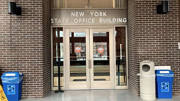 Glass double doors in a brick entryway beneath raised metal lettering, with recycling bins on both sides
