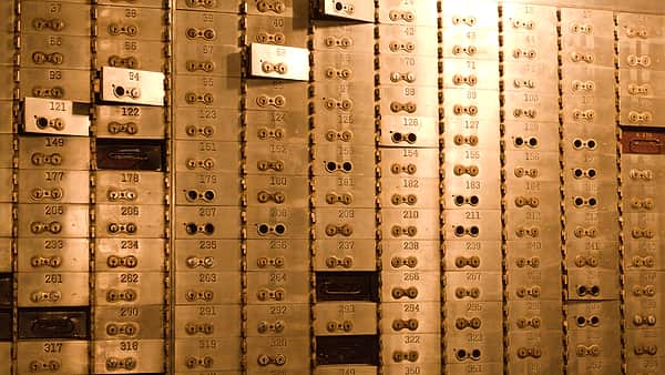 A wall of small numbered brass deposit boxes with twin keyholes, a few doors hanging open in warm light