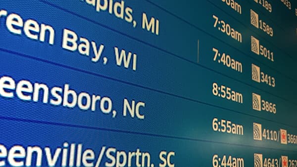 A close view of a blue electronic display board listing city and state names beside times in orange