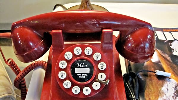 A glossy red desk telephone with a lettered dial pad and its handset resting in the cradle