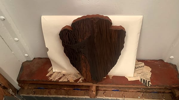 A thick carved wooden slab leaning against a large white envelope on a battered red painted ledge