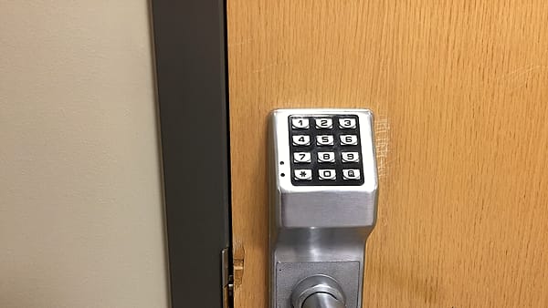 A brushed steel keypad with numbered buttons mounted above a round handle on a pale wooden door