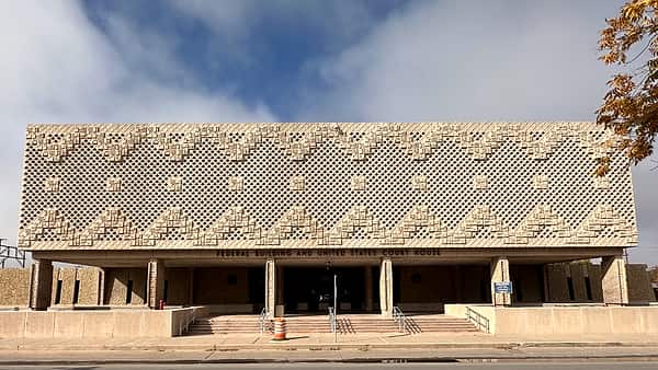A long low building fronted by a patterned pierced stone screen above concrete columns and entrance steps