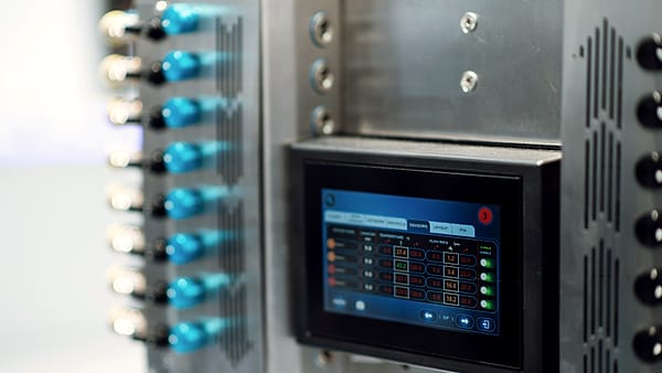 A lit color touchscreen set into a brushed steel cabinet beside two rows of blue-capped valve fittings