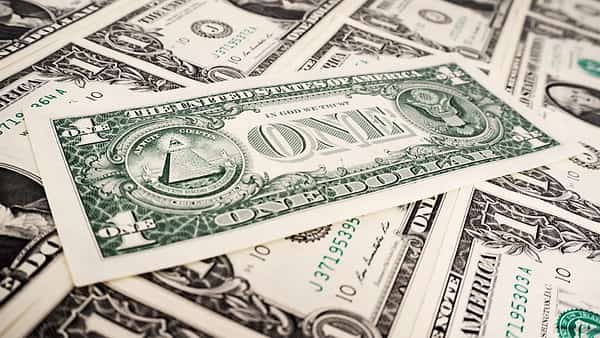 A one-dollar bill lying face up on a loose pile of identical bills, its pyramid and eagle in view