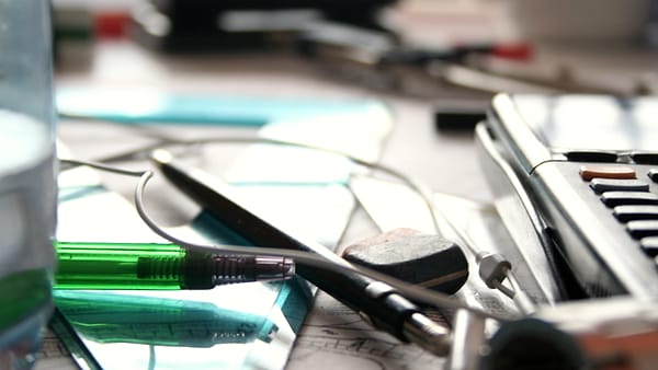 A close-up of a cluttered workbench with tweezers, a green pen, thin cables and pieces of cut glass