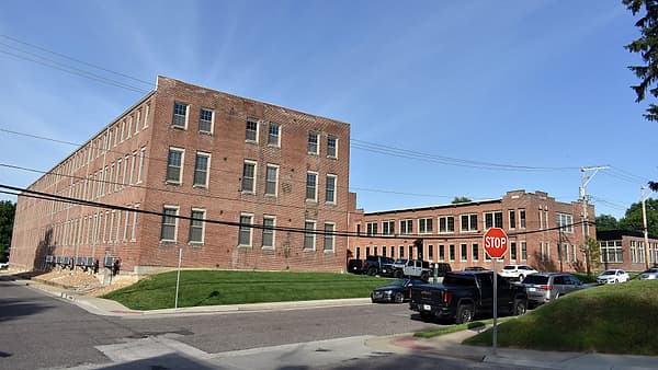 A large red brick industrial building beside a lot of parked pickup trucks, with a stop sign at the corner