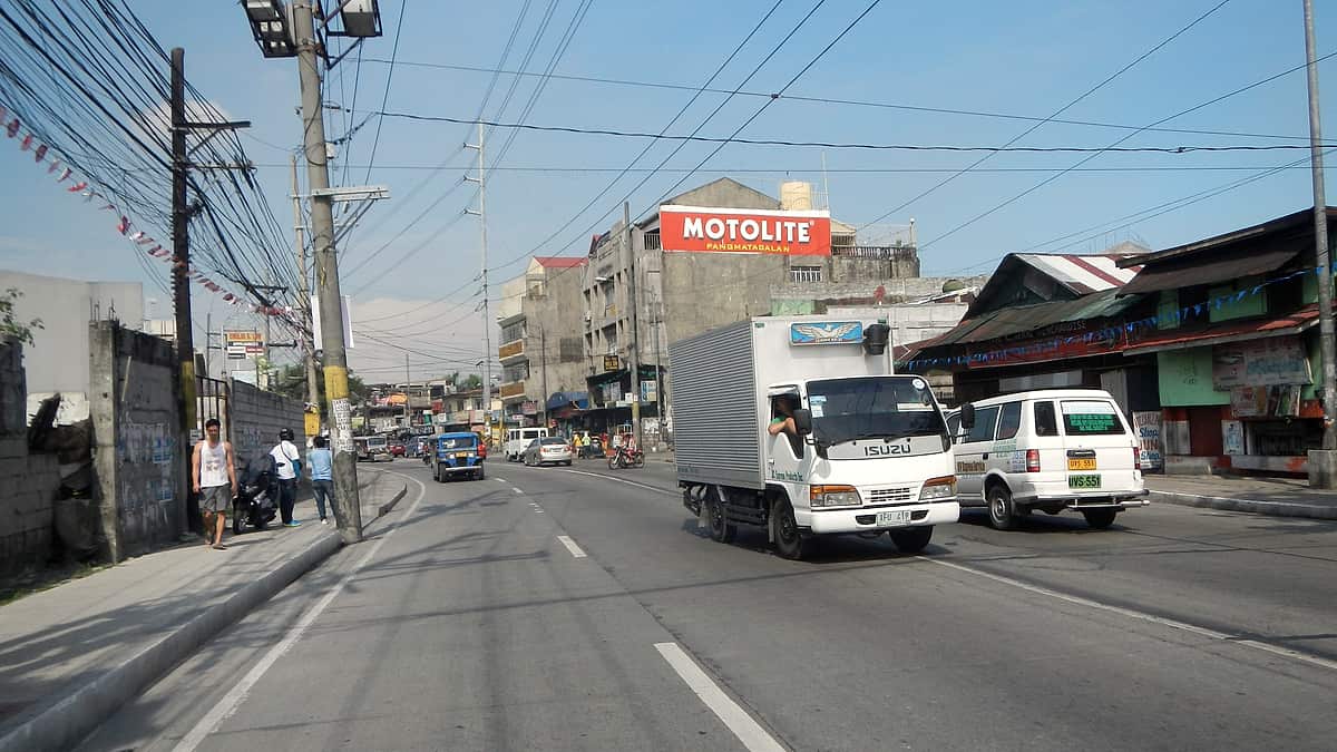 A row of small roadside shops and stacked goods along a wide highway shoulder.