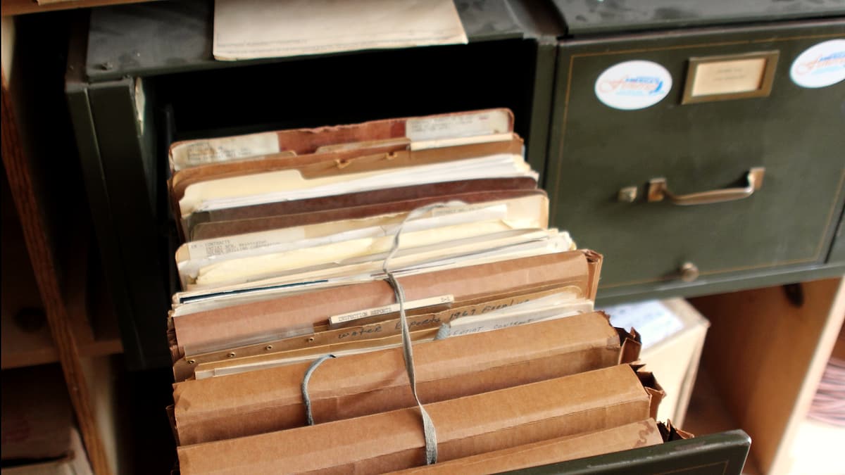 An open green metal filing drawer crammed with aged manila folders, several bundled with string