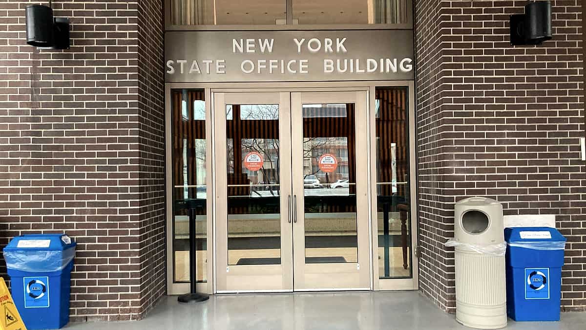 Glass double doors in a brick entryway beneath raised metal lettering, with recycling bins on both sides
