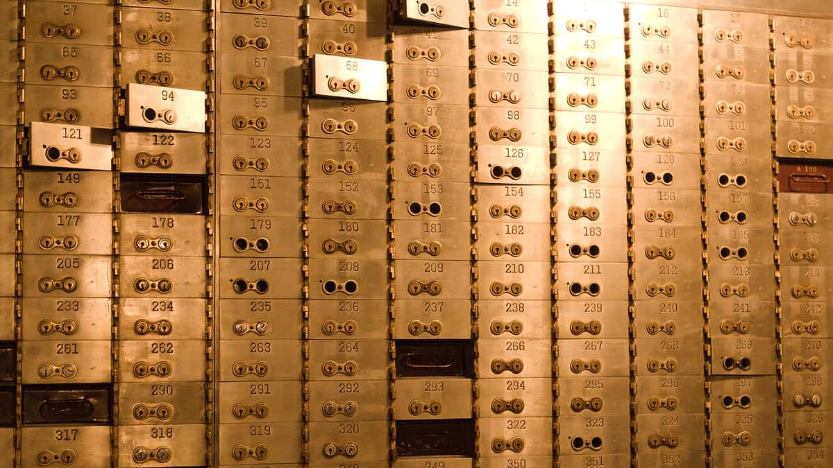 A wall of small numbered brass deposit boxes with twin keyholes, a few doors hanging open in warm light