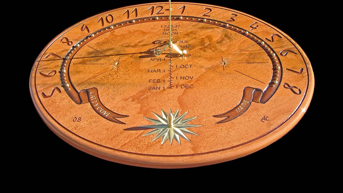 A round stone sundial face carved with hour numerals, a month scale and an inlaid gold compass star