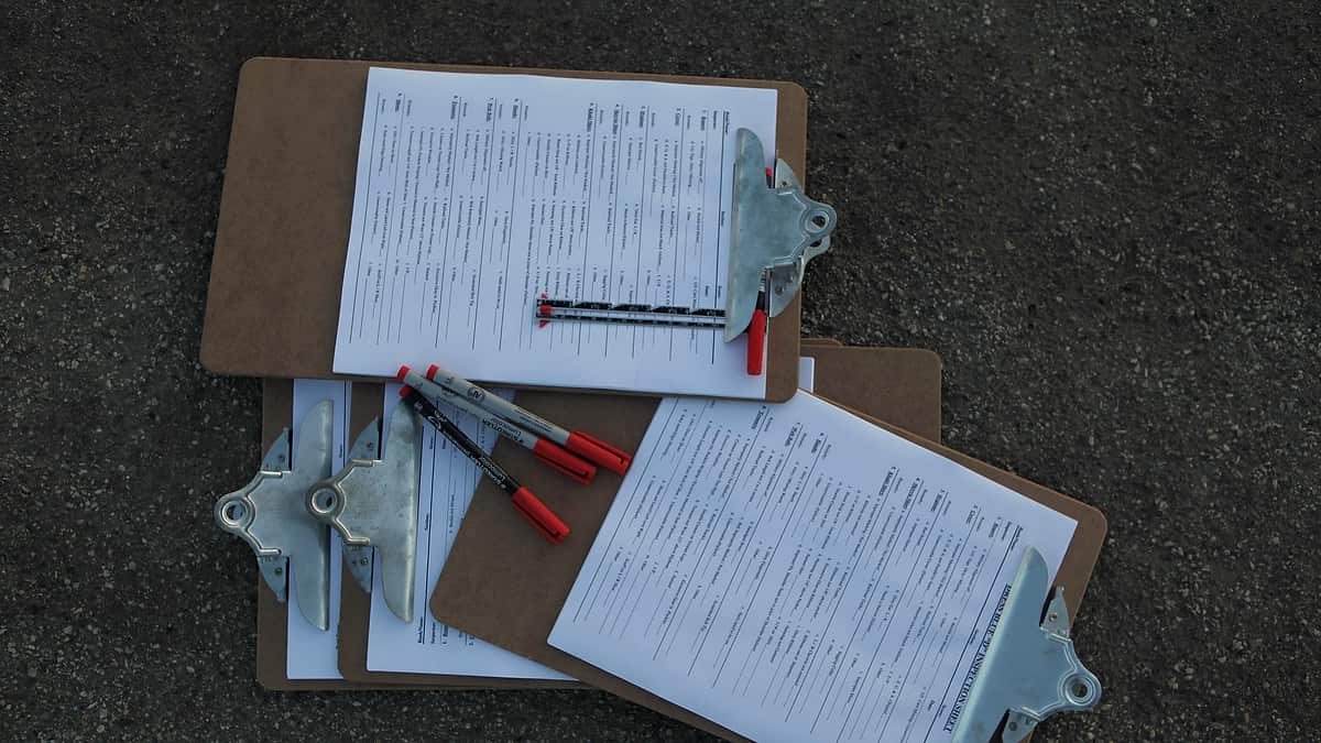 Three clipboards holding printed forms lying on gray asphalt with red-capped marker pens resting across them